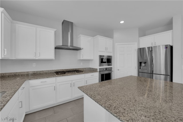 kitchen featuring white cabinetry, wall chimney exhaust hood, light stone counters, and appliances with stainless steel finishes