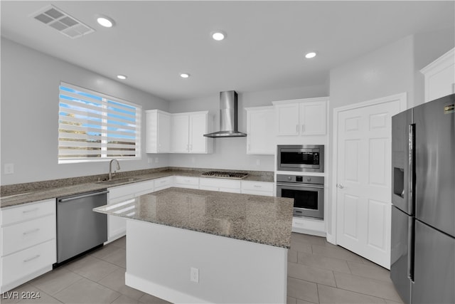 kitchen featuring white cabinets, appliances with stainless steel finishes, a center island, and wall chimney range hood