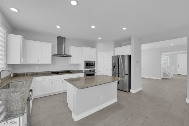 kitchen featuring sink, wall chimney exhaust hood, appliances with stainless steel finishes, a kitchen island, and light stone counters