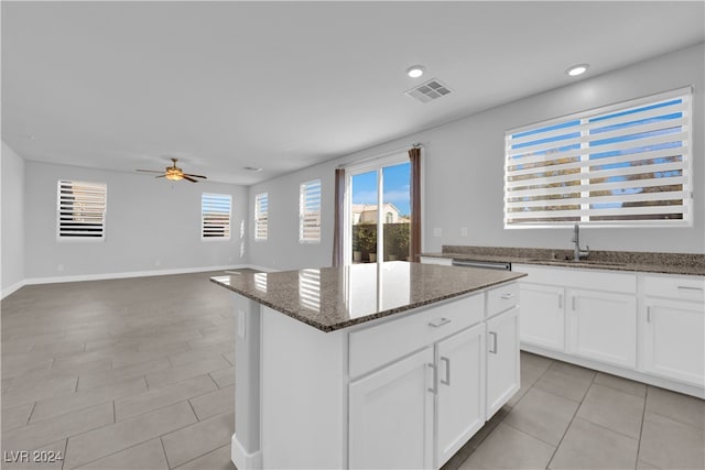 kitchen featuring white cabinetry, a center island, ceiling fan, sink, and dark stone countertops