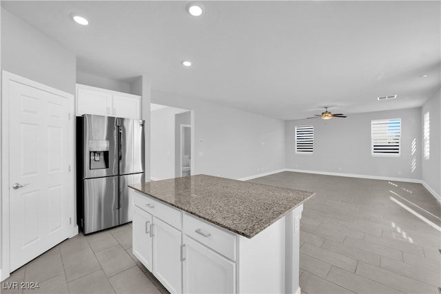 kitchen featuring a center island, stone counters, stainless steel fridge with ice dispenser, ceiling fan, and white cabinetry