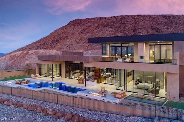 back house at dusk with a mountain view, a patio area, and a balcony