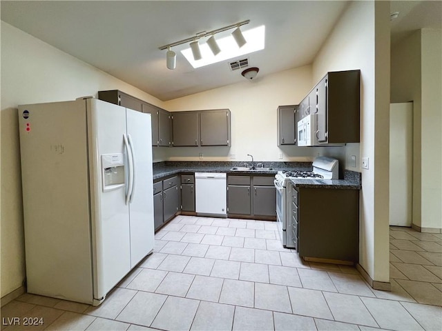 kitchen featuring rail lighting, lofted ceiling, sink, light tile patterned floors, and white appliances