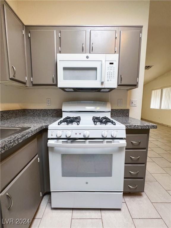 kitchen featuring gray cabinets, light tile patterned floors, white appliances, and dark stone counters