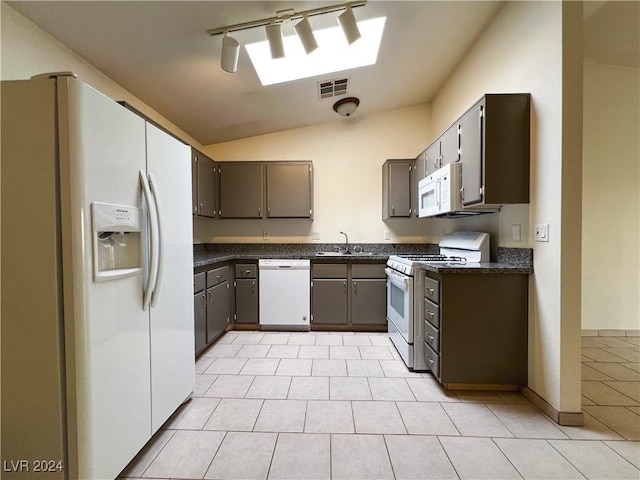 kitchen featuring lofted ceiling with skylight, light tile patterned flooring, sink, track lighting, and white appliances