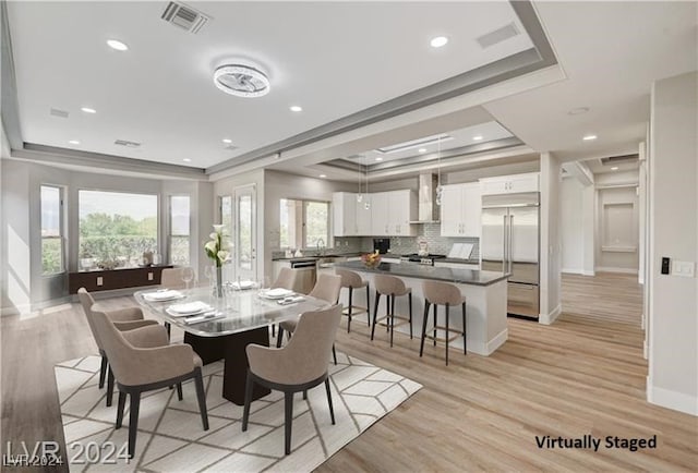 dining space with a tray ceiling, light hardwood / wood-style flooring, and a healthy amount of sunlight