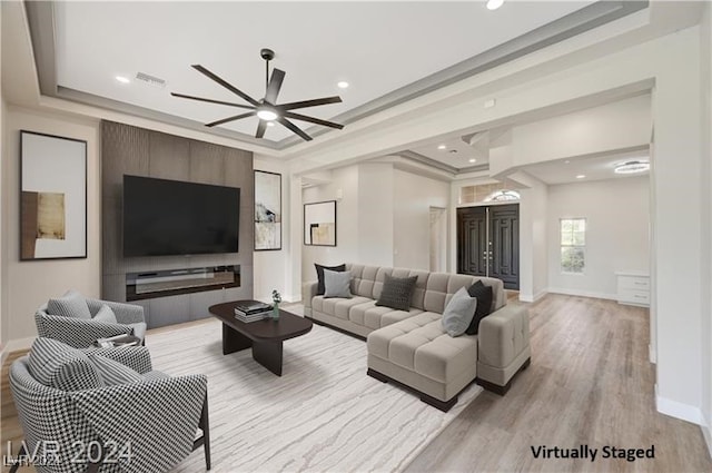 living room featuring ornamental molding, a tray ceiling, ceiling fan, and light hardwood / wood-style floors