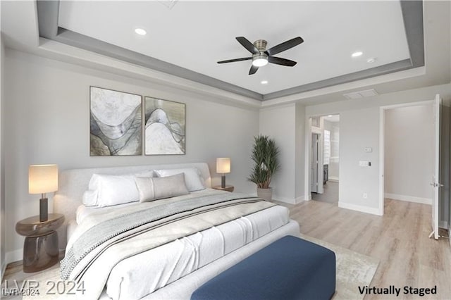 bedroom with ceiling fan, light wood-type flooring, connected bathroom, and a tray ceiling