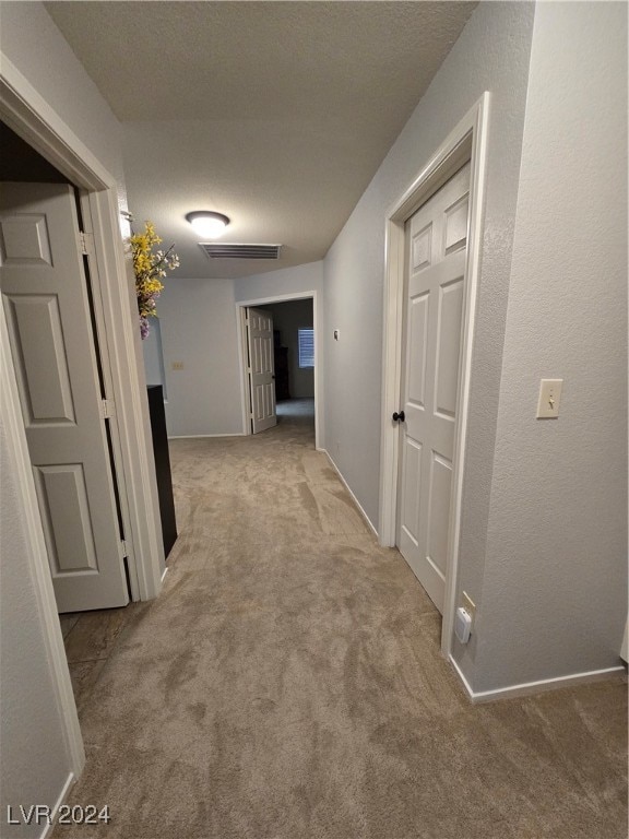 corridor with a textured ceiling and light colored carpet