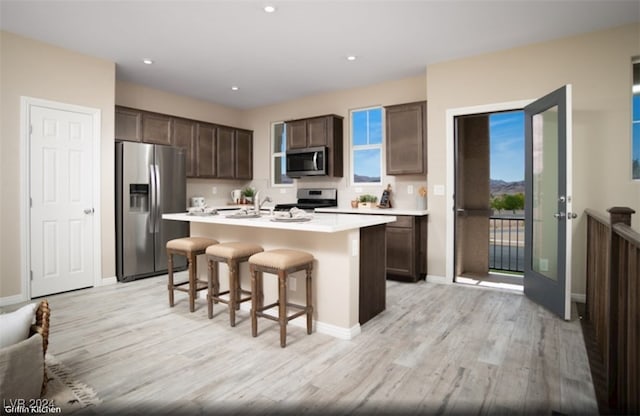 kitchen with stainless steel appliances, a kitchen breakfast bar, a center island with sink, dark brown cabinets, and light wood-type flooring