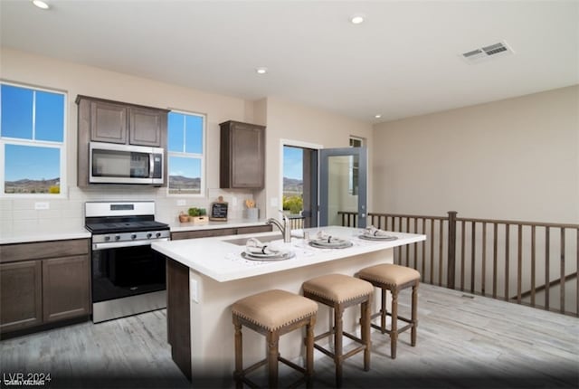 kitchen with sink, an island with sink, light hardwood / wood-style flooring, and appliances with stainless steel finishes