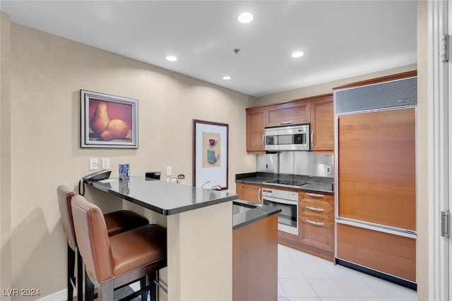 kitchen with white oven, kitchen peninsula, stovetop, paneled built in refrigerator, and a breakfast bar