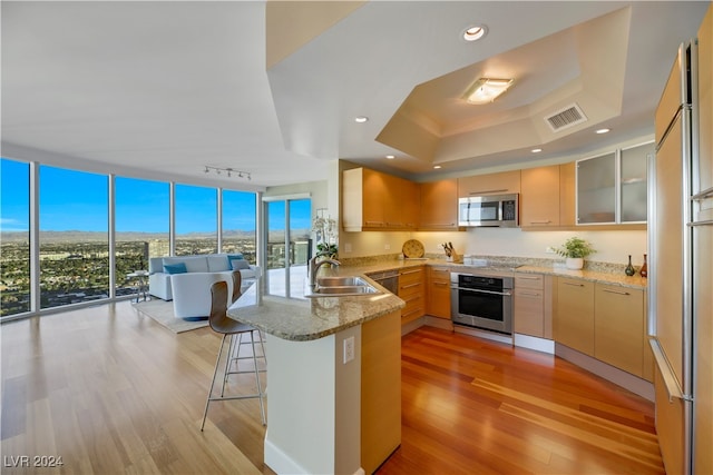 kitchen featuring light stone countertops, kitchen peninsula, a kitchen bar, appliances with stainless steel finishes, and light wood-type flooring