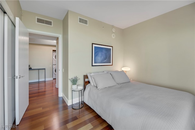 bedroom featuring dark wood-type flooring and stacked washer / dryer