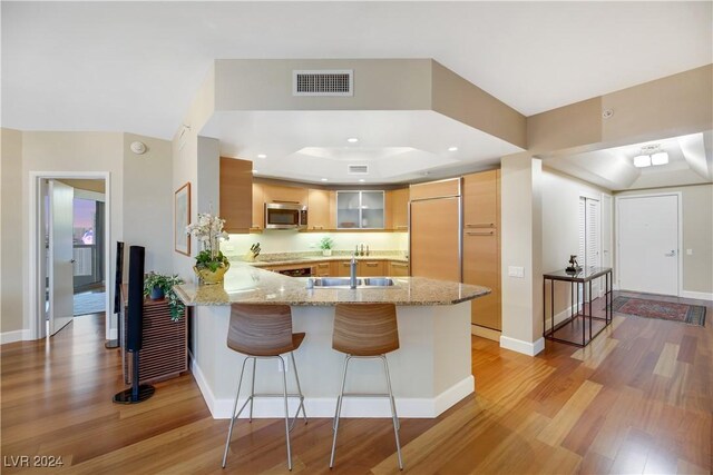 kitchen with kitchen peninsula, light brown cabinetry, paneled refrigerator, a raised ceiling, and light hardwood / wood-style floors