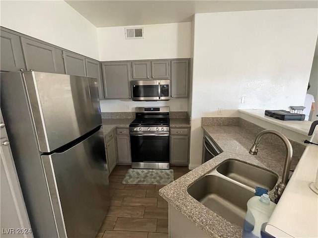 kitchen with appliances with stainless steel finishes, gray cabinets, dark hardwood / wood-style floors, and sink