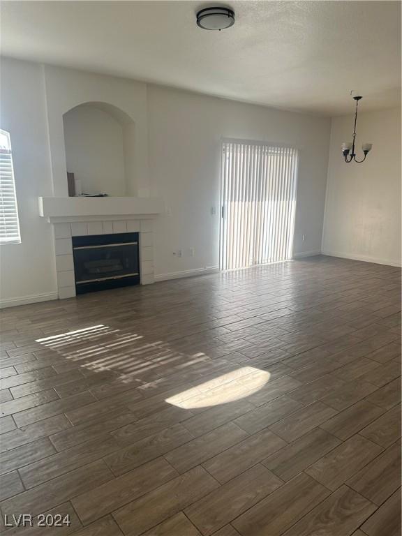 unfurnished living room with a notable chandelier, dark hardwood / wood-style flooring, and a tiled fireplace