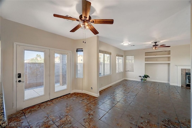 unfurnished living room with visible vents, baseboards, a ceiling fan, a tiled fireplace, and built in shelves