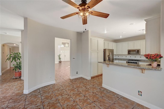 kitchen featuring arched walkways, light stone countertops, stainless steel appliances, a peninsula, and decorative backsplash