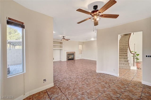 unfurnished living room featuring a tile fireplace, ceiling fan, baseboards, and stairs