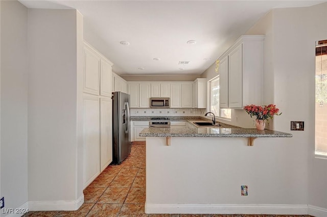 kitchen featuring light stone counters, a breakfast bar, a peninsula, stainless steel appliances, and a sink