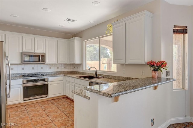 kitchen featuring a peninsula, stainless steel appliances, a kitchen bar, white cabinetry, and a sink