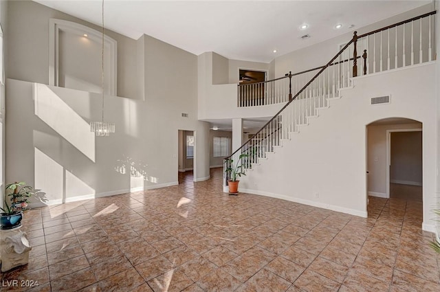 unfurnished living room featuring arched walkways, visible vents, baseboards, and stairs