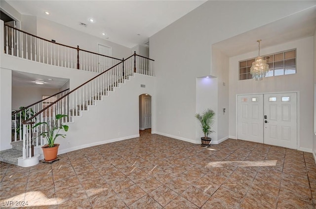 entryway featuring arched walkways, a notable chandelier, a high ceiling, baseboards, and stairs