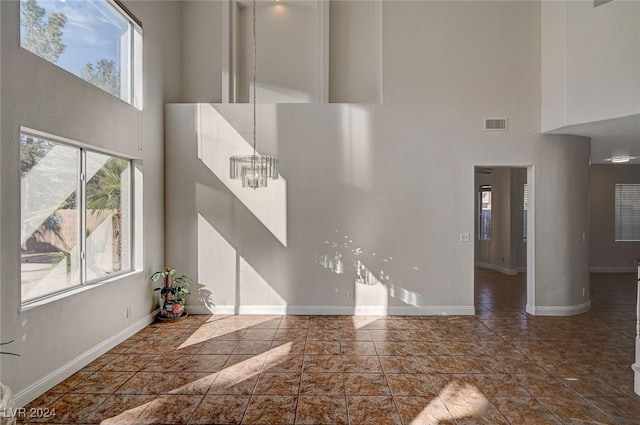 unfurnished living room featuring a high ceiling, an inviting chandelier, visible vents, and baseboards