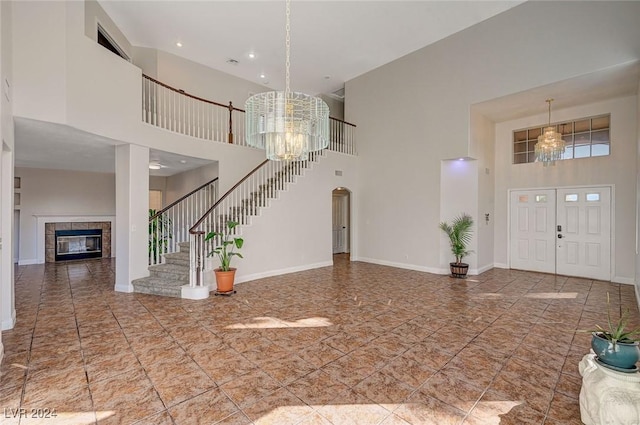 entryway with a fireplace, a towering ceiling, baseboards, stairway, and an inviting chandelier