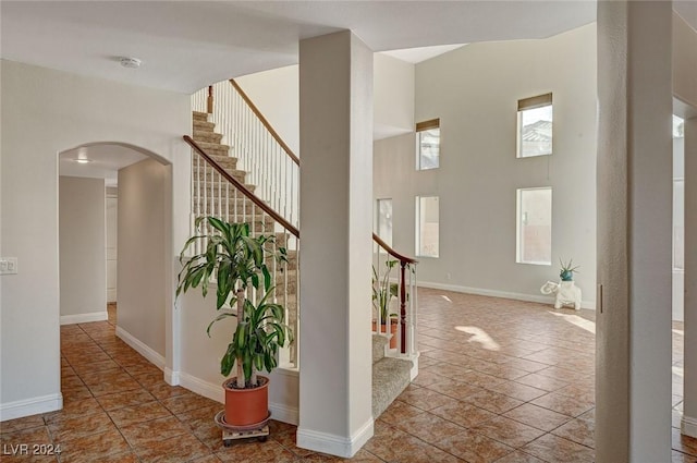 interior space featuring arched walkways, a high ceiling, baseboards, and tile patterned floors