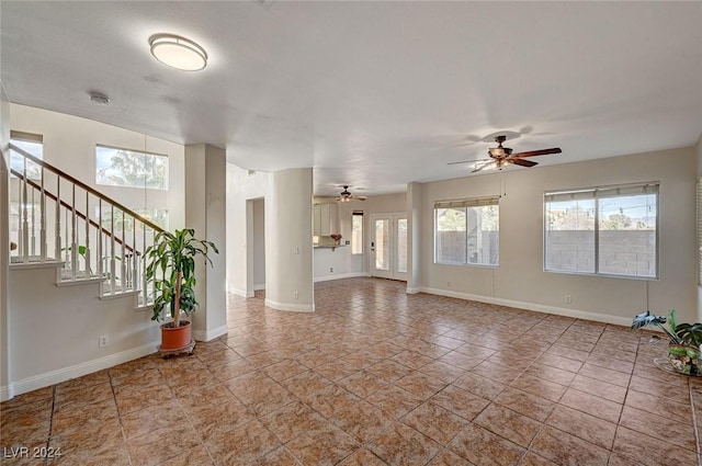 unfurnished living room featuring stairs, baseboards, and a ceiling fan