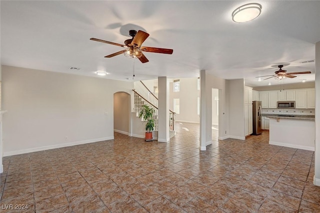 unfurnished living room with arched walkways, ceiling fan, stairs, and baseboards