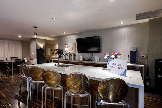 kitchen featuring sink, dark wood-type flooring, light stone counters, decorative light fixtures, and a center island with sink