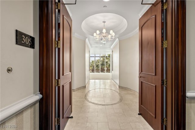 hallway with a notable chandelier, light tile patterned flooring, ornamental molding, and a tray ceiling