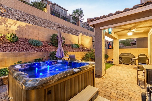 patio terrace at dusk with a hot tub, area for grilling, and ceiling fan