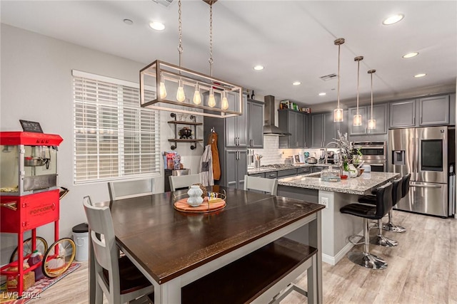 kitchen with gray cabinetry, light stone counters, appliances with stainless steel finishes, pendant lighting, and a kitchen island with sink