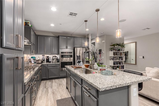 kitchen featuring gray cabinets, a kitchen island with sink, stainless steel appliances, light stone countertops, and decorative light fixtures