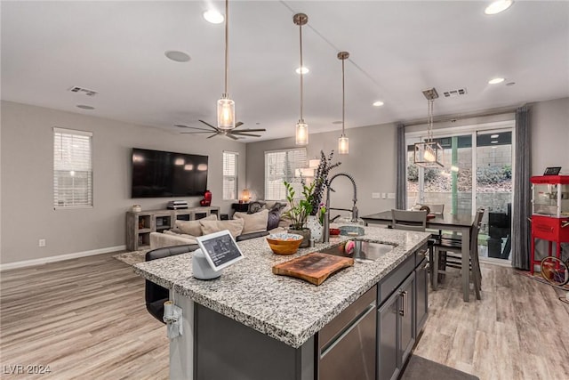 kitchen with hanging light fixtures, an island with sink, light stone countertops, and sink