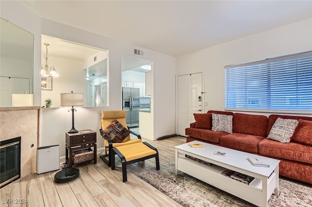 living room with a notable chandelier, light wood-type flooring, and a tile fireplace