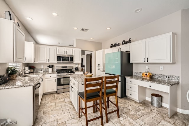 kitchen featuring light stone countertops, stainless steel appliances, a kitchen island, sink, and white cabinetry