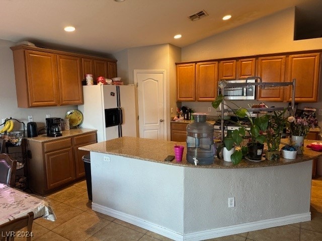 kitchen featuring light tile patterned floors, a center island with sink, vaulted ceiling, and white fridge with ice dispenser