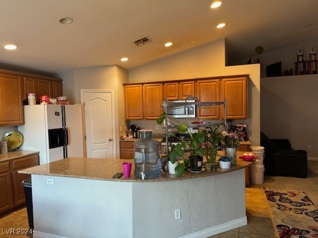 kitchen with white fridge with ice dispenser, light stone counters, an island with sink, vaulted ceiling, and light tile patterned floors