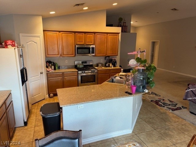 kitchen with a center island with sink, light tile patterned floors, stainless steel appliances, and vaulted ceiling