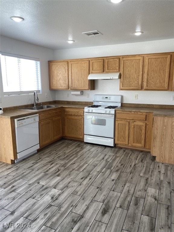 kitchen with light wood-type flooring, a textured ceiling, white appliances, and sink