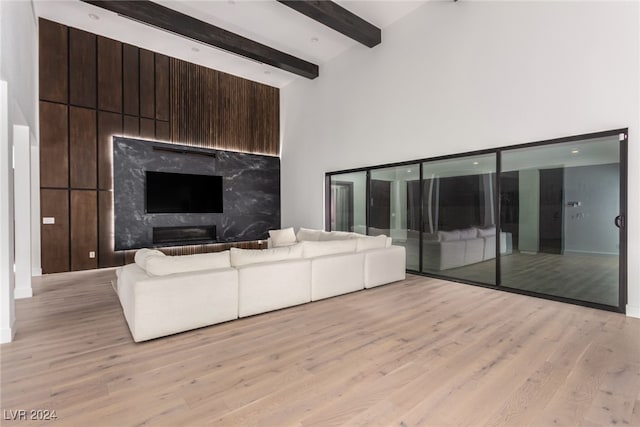 unfurnished living room featuring a high end fireplace, beam ceiling, light wood-type flooring, and a high ceiling