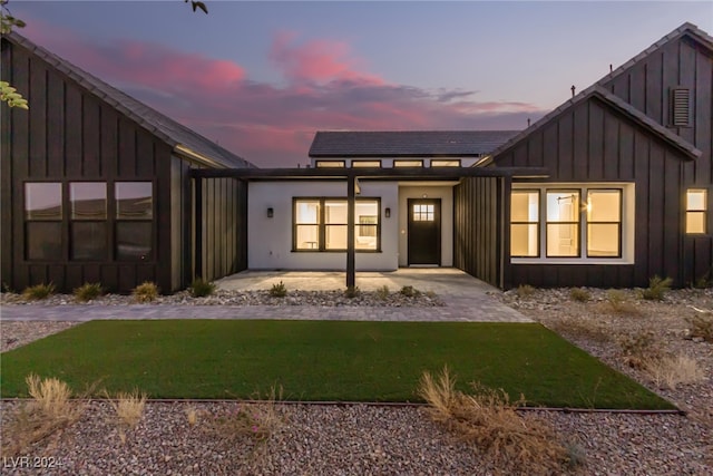 back house at dusk featuring a lawn and a patio area