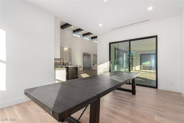 dining space featuring beamed ceiling, a towering ceiling, and light hardwood / wood-style flooring