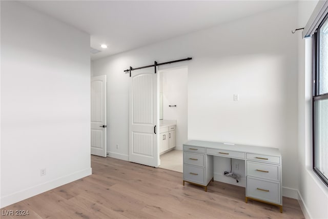 unfurnished office featuring a barn door and light hardwood / wood-style flooring