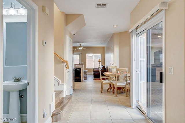 corridor featuring baseboards, visible vents, light tile patterned flooring, a sink, and stairs